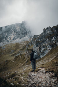 Rear view of man standing on rock against mountain and sky