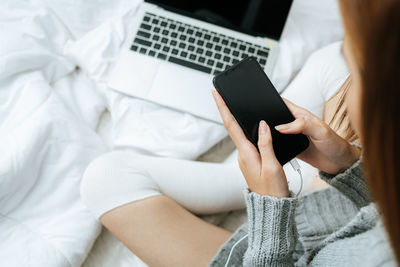 Midsection of woman using mobile phone while lying on bed at home