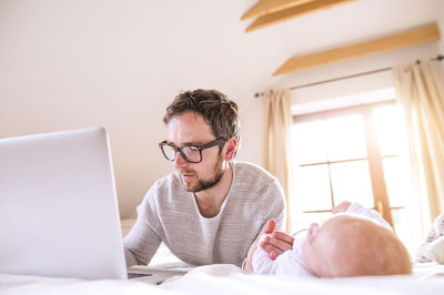 Father with baby lying on bed using laptop