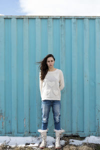 Portrait of a smiling young woman standing against blue wall