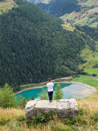 High angle view of boy standing on stone against lake by mountains