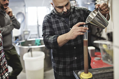 Coworkers looking at man pouring beer in container at brewery