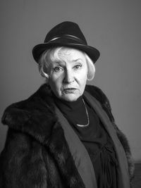 Close-up portrait of senior woman wearing fur coat against gray background