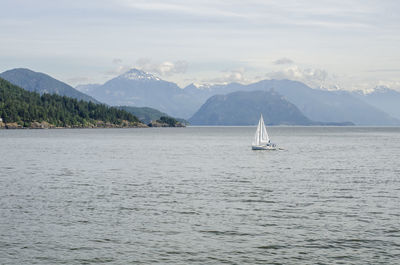 Sailboat sailing on sea against mountains