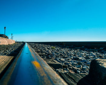 Surface level of railroad tracks against clear blue sky