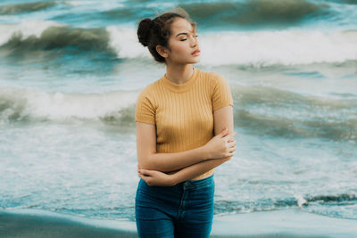 Young woman standing with arms crossed at beach