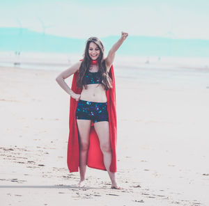 Smiling young woman wearing red cape standing at beach