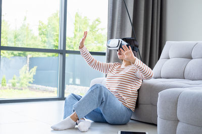 Young woman wearing virtual reality sitting on floor at home