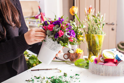 Midsection of woman holding flower vase on table