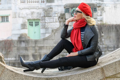 A blonde lady with a red scarf is sitting on the wall and enjoying the autumn sun.