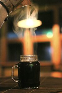 Cropped image of coffee pot pouring drink in mason jar on table