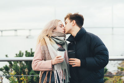 Young couple kissing while standing by railing
