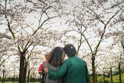 Rear view of mother and daughter hugging against blooming trees