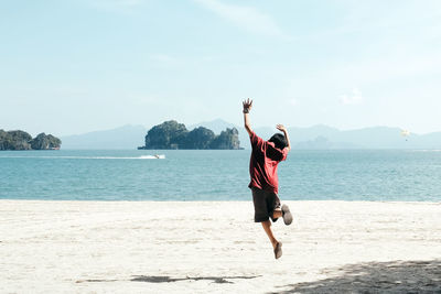 Rear view of boy jumping on beach against sky