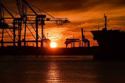 Profile of a large ship and container cranes at sunset
