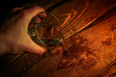 Cropped hand of person pouring water from glass on wooden table