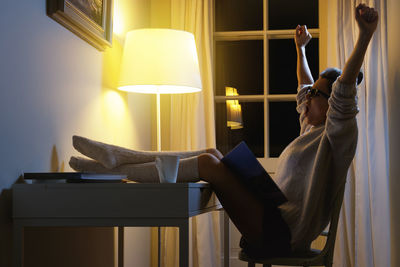 Woman with arms raised yawning at home