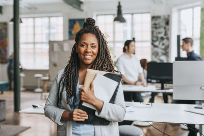 Portrait of smiling businesswoman with braided hair holding files at office