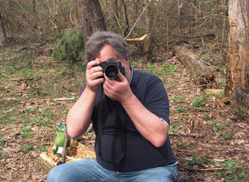 Young man photographing while sitting on land