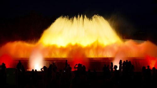 Silhouette people with illuminated fountain against sky at night