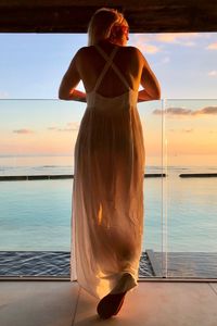 Beautiful girl in white dress looks out at sea at sunset