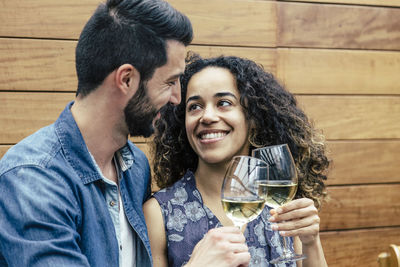 Smiling young couple toasting wine against wooden wall