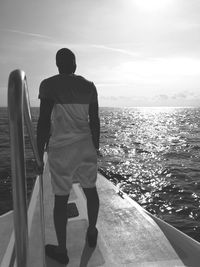 Rear view of man standing in boat on sea against sky