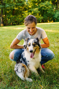 Happy young woman spending time with lovely spotted australian shepherd dog in green meadow on