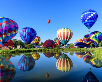 Hot air balloons flying over lake against clear blue sky