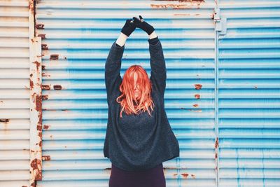 Woman standing with arms raised against blue weathered shutter