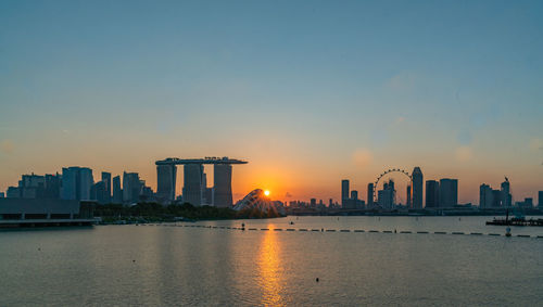 Sea and buildings against sky during sunset