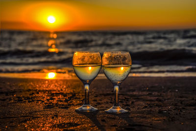 Wine glasses on glass against sea during sunset