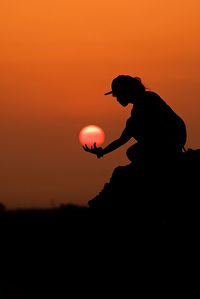 Optical illusion of silhouette woman holding sun during sunrise