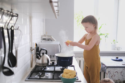 Cute toddler child in kitchen by stove helps mom cook, bright interior of kitchen