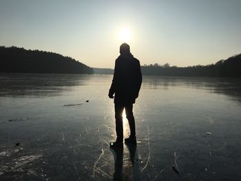 Rear view of silhouette man standing at frozen lake against sky during sunset