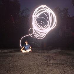 Man with illuminated wire wools sitting on land at night