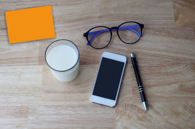 High angle view of smart phone with eyeglasses pen and milk in glass on table