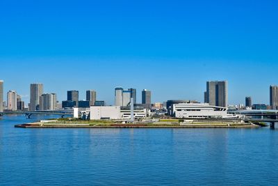 Sea by cityscape against clear blue sky