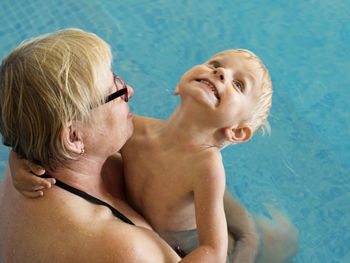 Rear view of grandmother with shirtless grandson swimming in pool