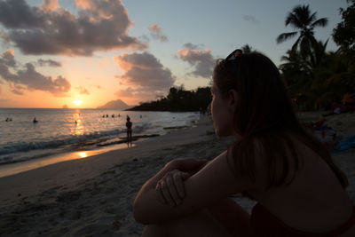 Side view of woman sitting at beach during sunset