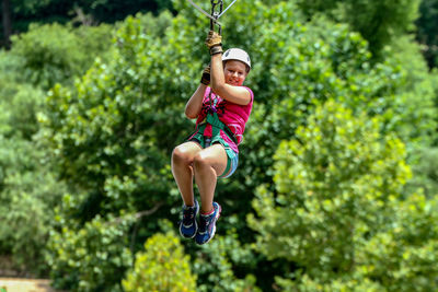 Full length of girl zip lining against trees