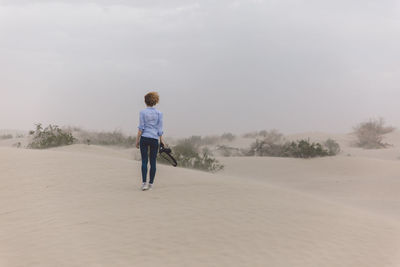 Rear view of man walking on landscape against sky