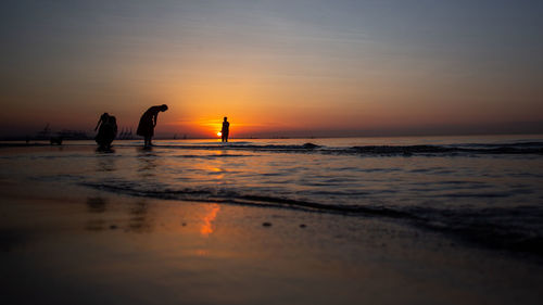 Silhouette people on beach against sky during sunset