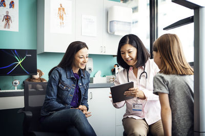 Happy female doctor showing tablet computer to family in clinic