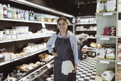 Portrait of smiling female owner with hand on hip in deli store