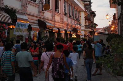 People walking on illuminated street amidst buildings in city at dusk