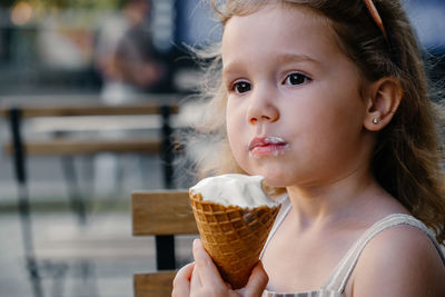 Toddler child eating cone ice cream outside near cafe. cute blonde caucasian girl licking frozen