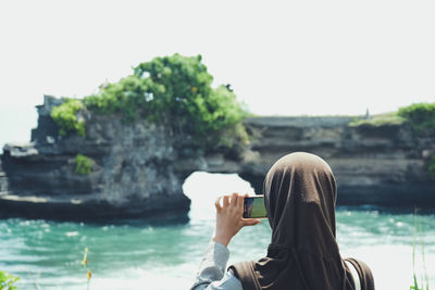 Rear view of man using mobile phone against sky