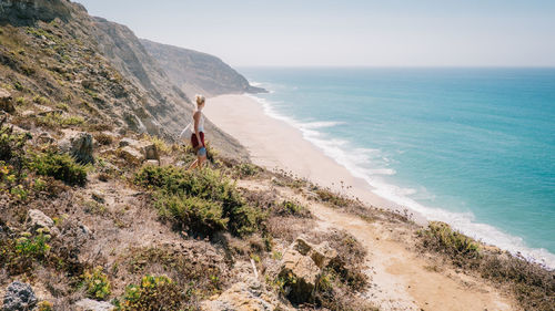 Woman walking on cliff by sea against clear sky