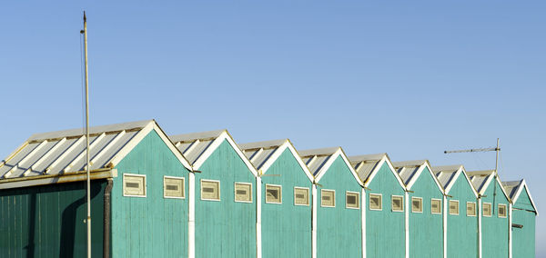 Beach huts against buildings against clear blue sky